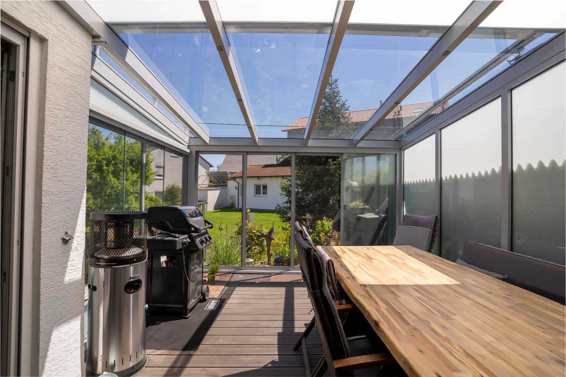 Überdachte Terrasse mit Holztisch, Stühlen und Grill, mit Blick in den Garten.