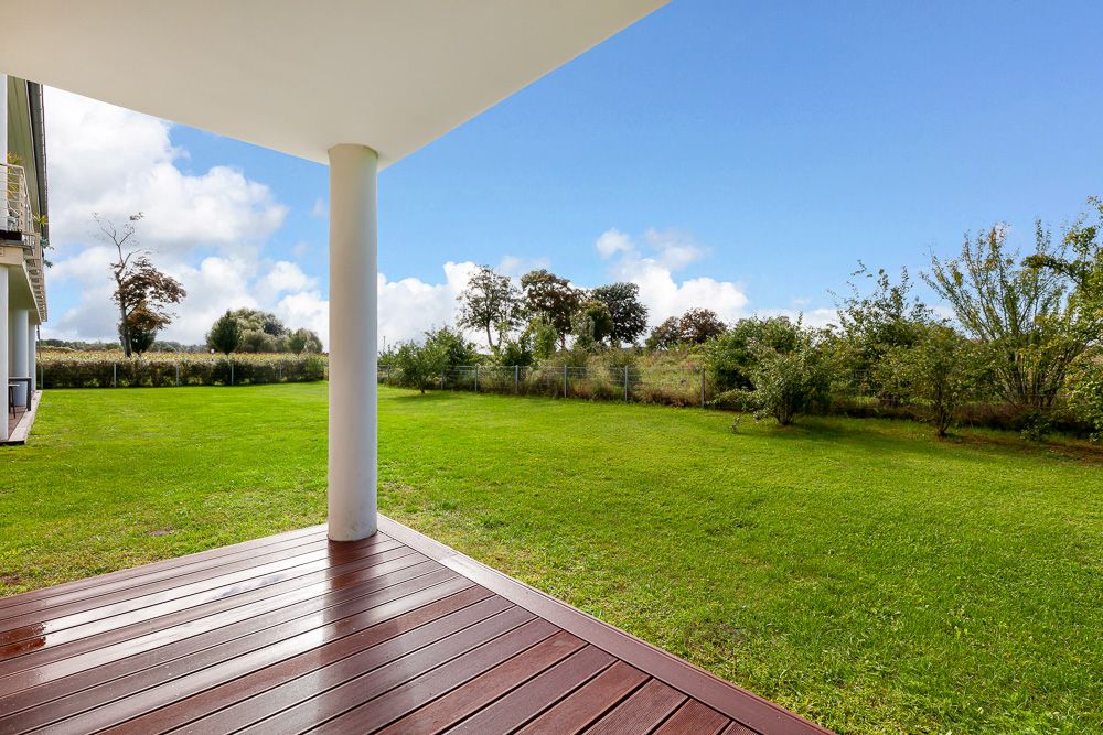 Überdachte Terrasse mit Holzboden blickt auf großen grünen Garten mit Bäumen.