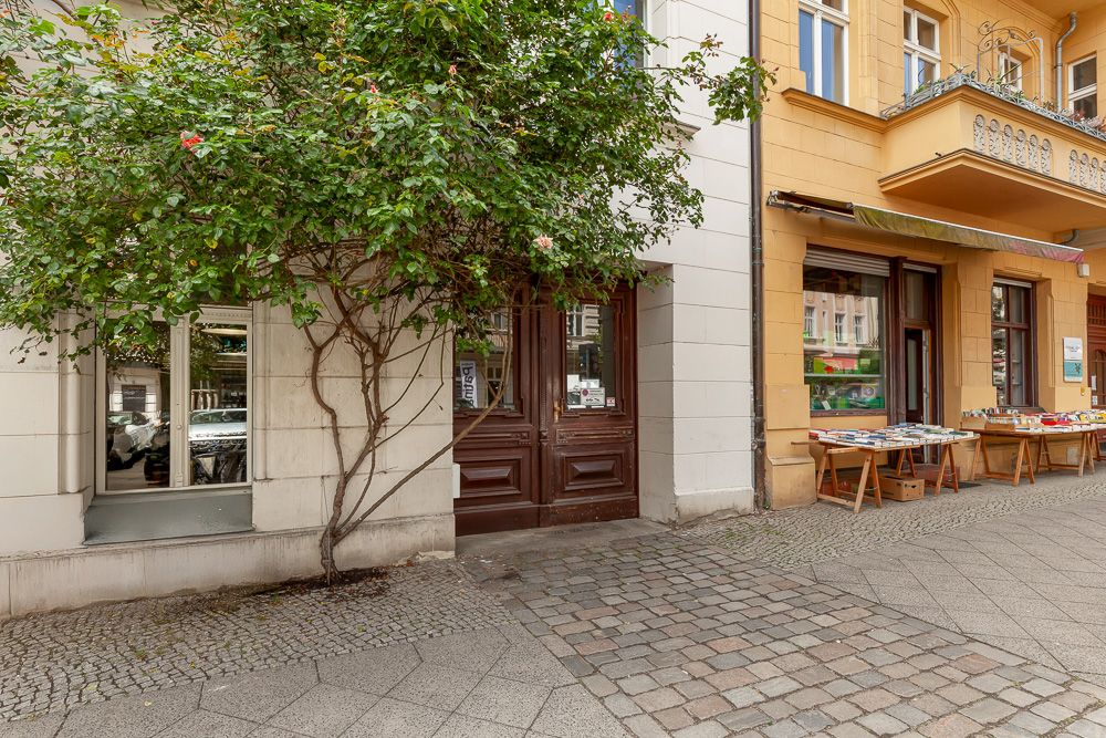 Eingangstür mit Baum davor und Fahrradständer auf gepflastertem Gehweg vor Wohnhaus.