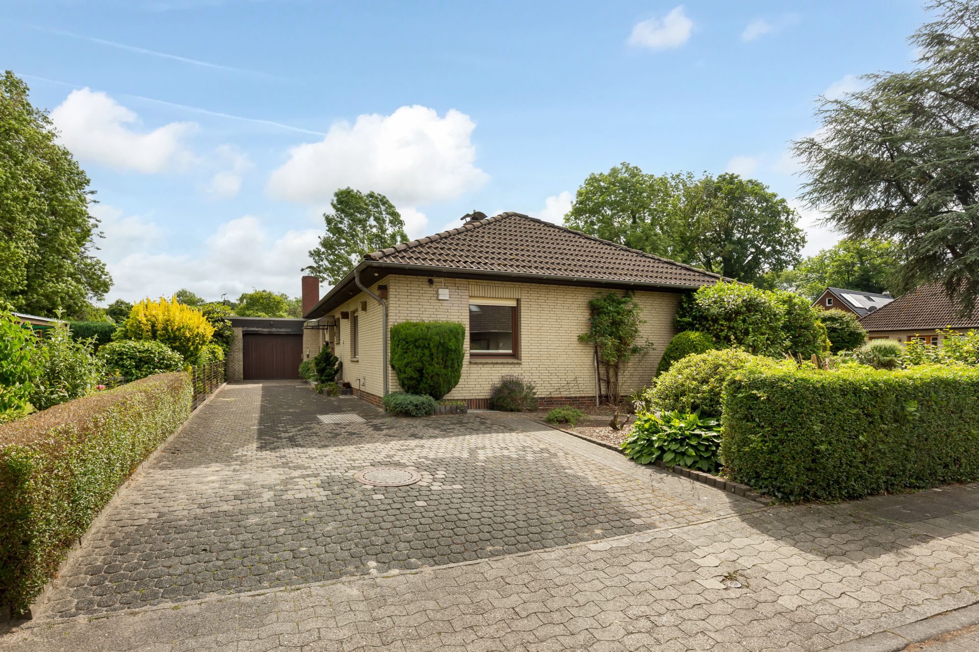 Einfamilienhaus mit braunem Dach, gepflasterter Einfahrt und gepflegtem Garten.