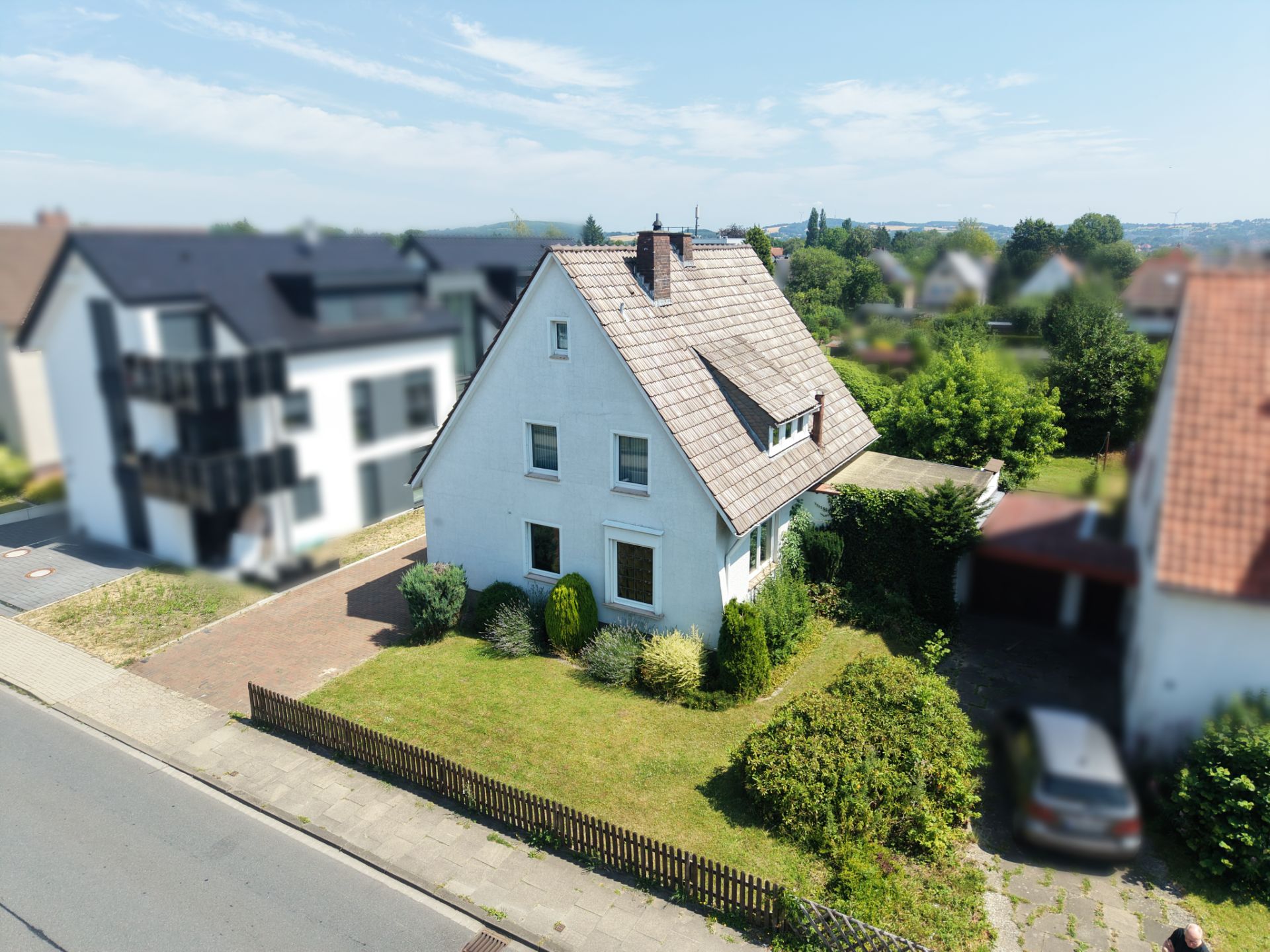 Weißes Einfamilienhaus mit Garten, Zaun und Auffahrt, an einer ruhigen Straße gelegen.