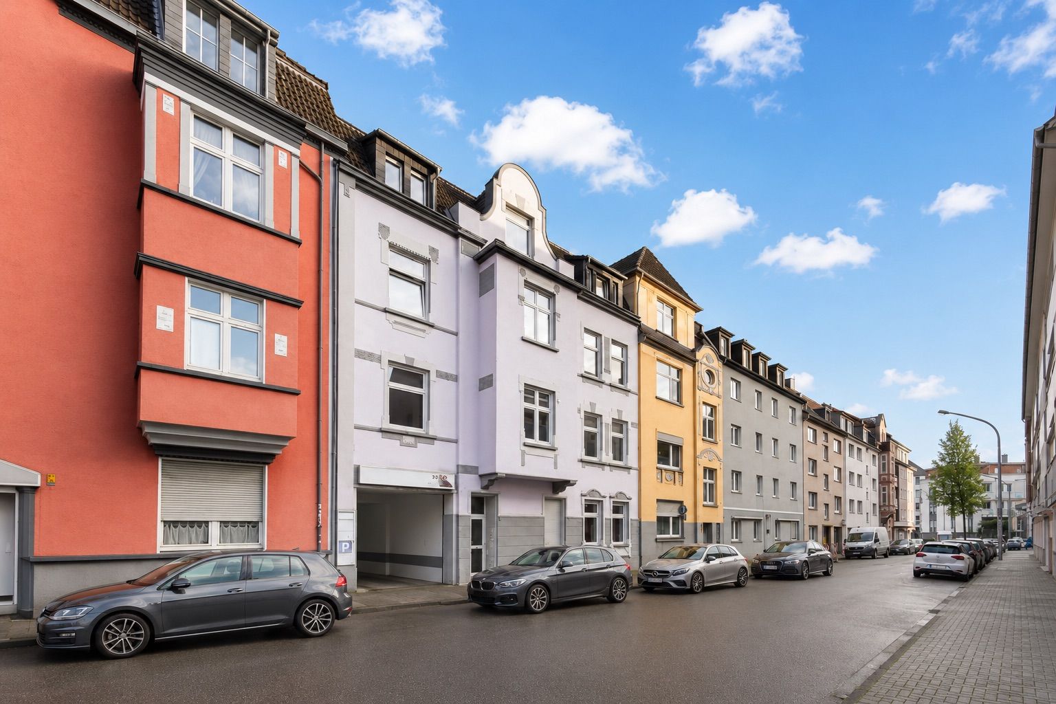Reihe von bunten Wohnhäusern an einer Straße mit geparkten Autos und blauem Himmel.