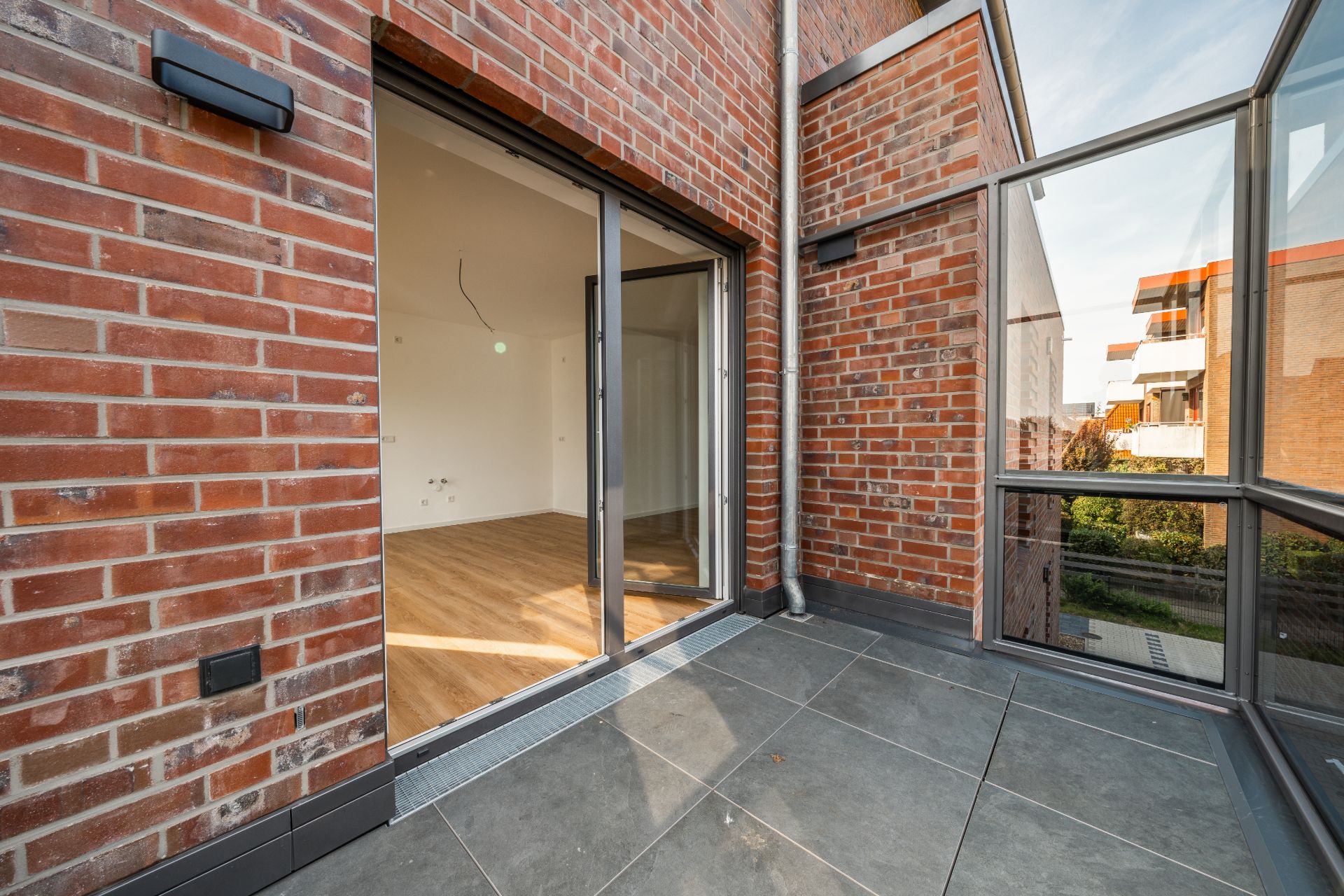 Moderner Balkon mit Fliesenboden und Blick in ein helles Zimmer durch eine Glas-Schiebetür.