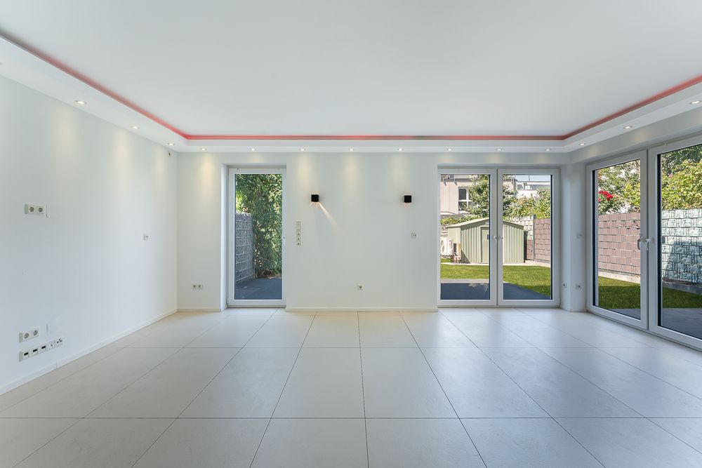 Heller, leerer Raum mit großen Fenstern und Blick auf einen Garten.