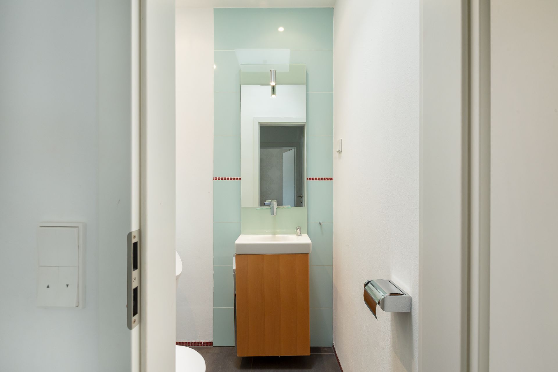 Modernes Badezimmer mit Waschbecken, Spiegel und Holzmöbel, gesehen durch die Tür.