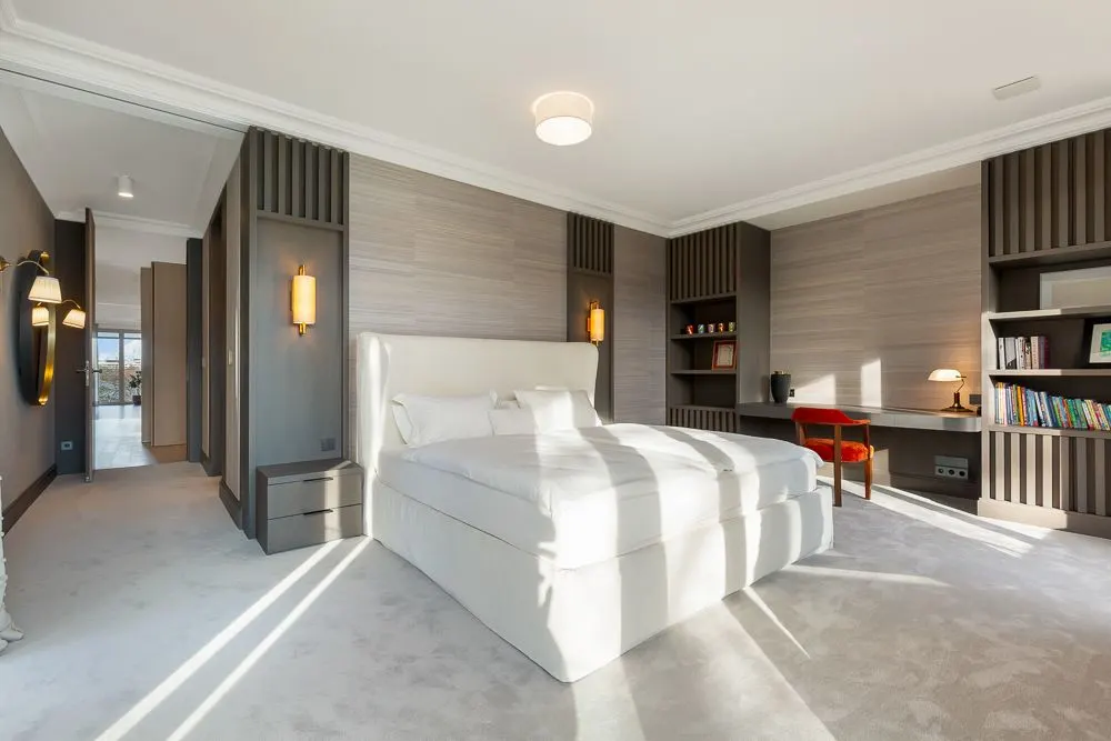 Modernes Schlafzimmer mit großem Bett, Schreibtisch, Stuhl und Bücherregalen an der Wand.