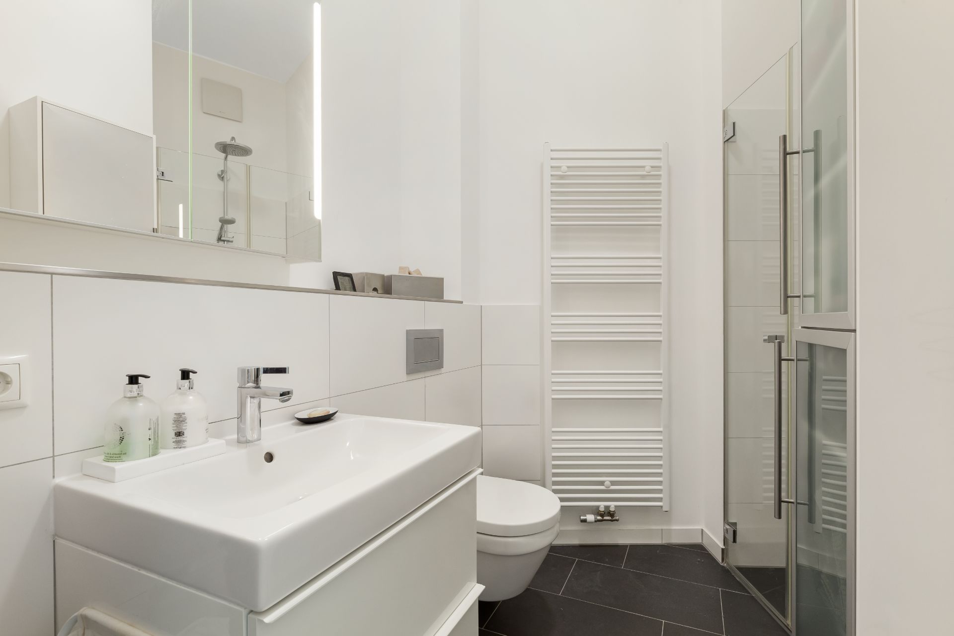 Modernes Badezimmer mit Waschbecken, Toilette, Handtuchheizkörper und Glasdusche.