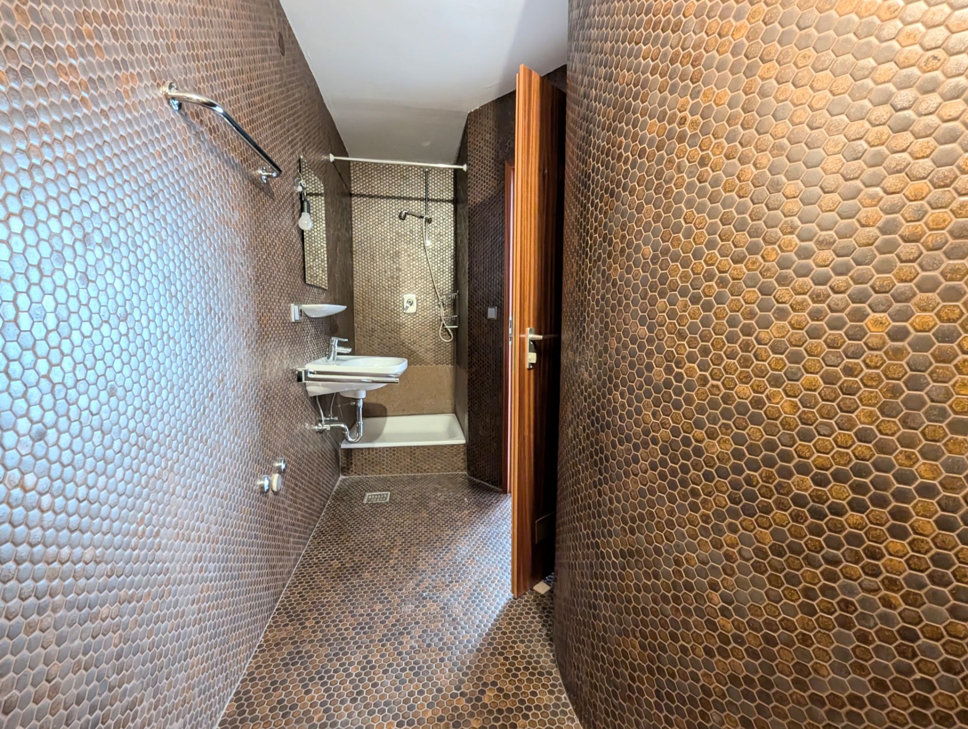 Badezimmer mit braunen Fliesen, Waschbecken, Spiegel, Dusche und Handtuchhalter.