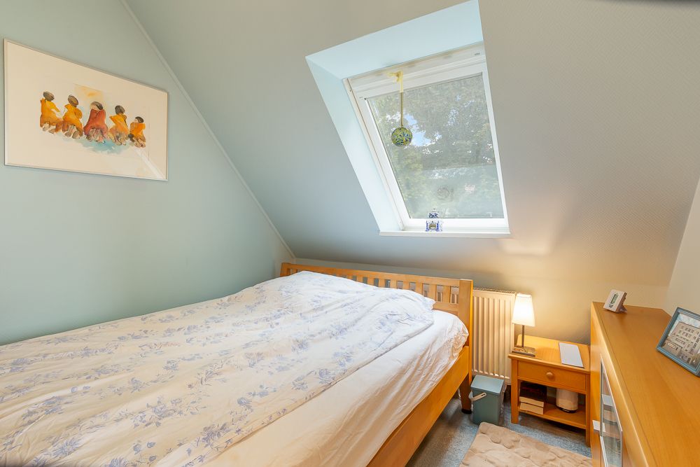 Kleines Schlafzimmer mit Holzbett, Dachfenster und Nachttisch mit Lampe.