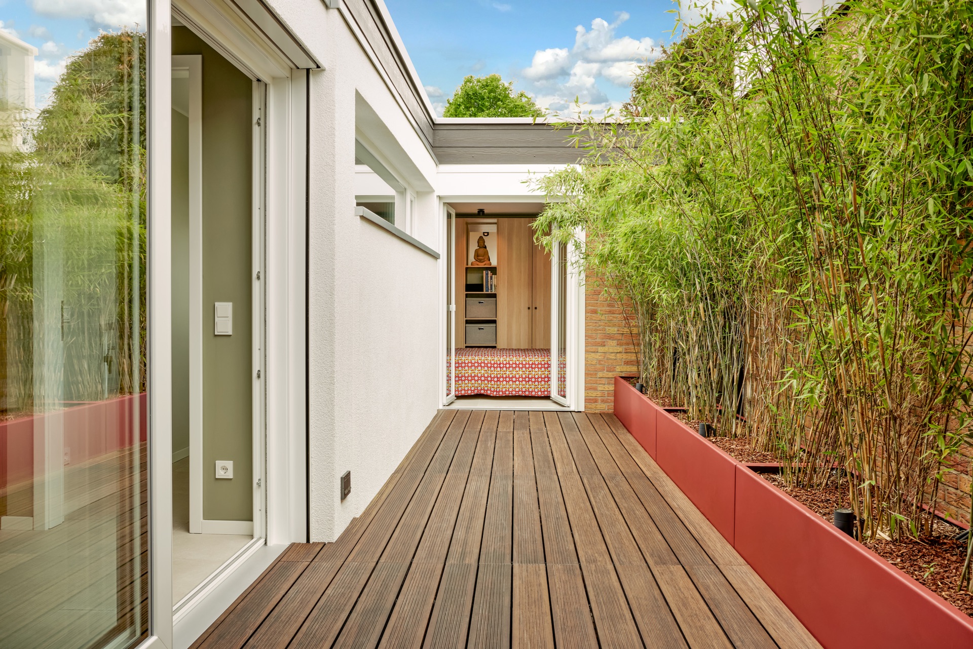 Holzterrasse mit Pflanzkübeln und Zugang zu Innenräumen eines Wohnhauses.
