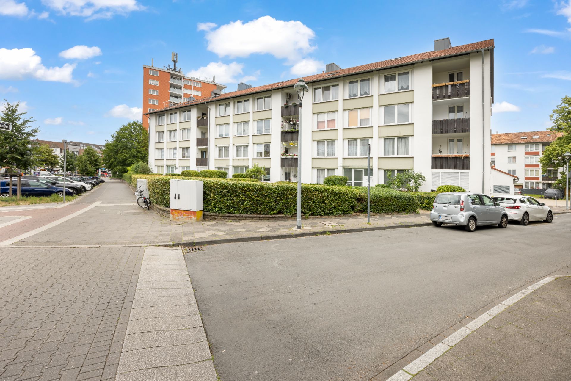 Mehrstöckiges Wohngebäude mit Balkonen, geparkten Autos und Gehweg im Vordergrund.