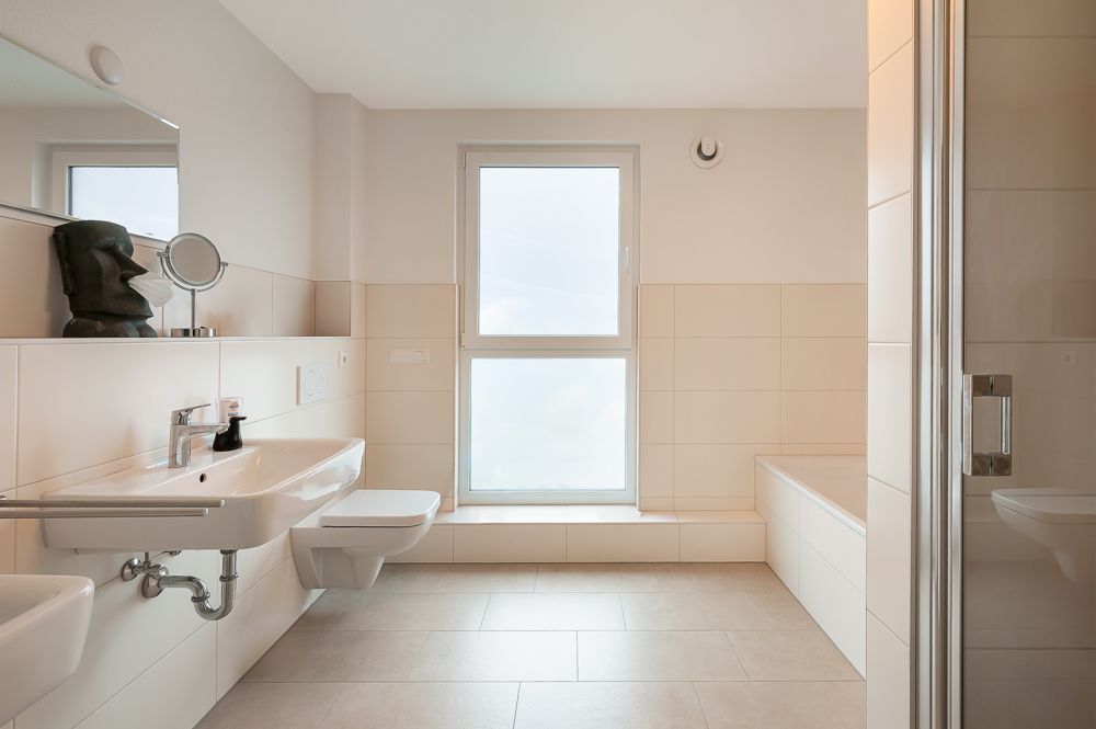 Helles Badezimmer mit Waschbecken, Toilette, Badewanne und großem Fenster.