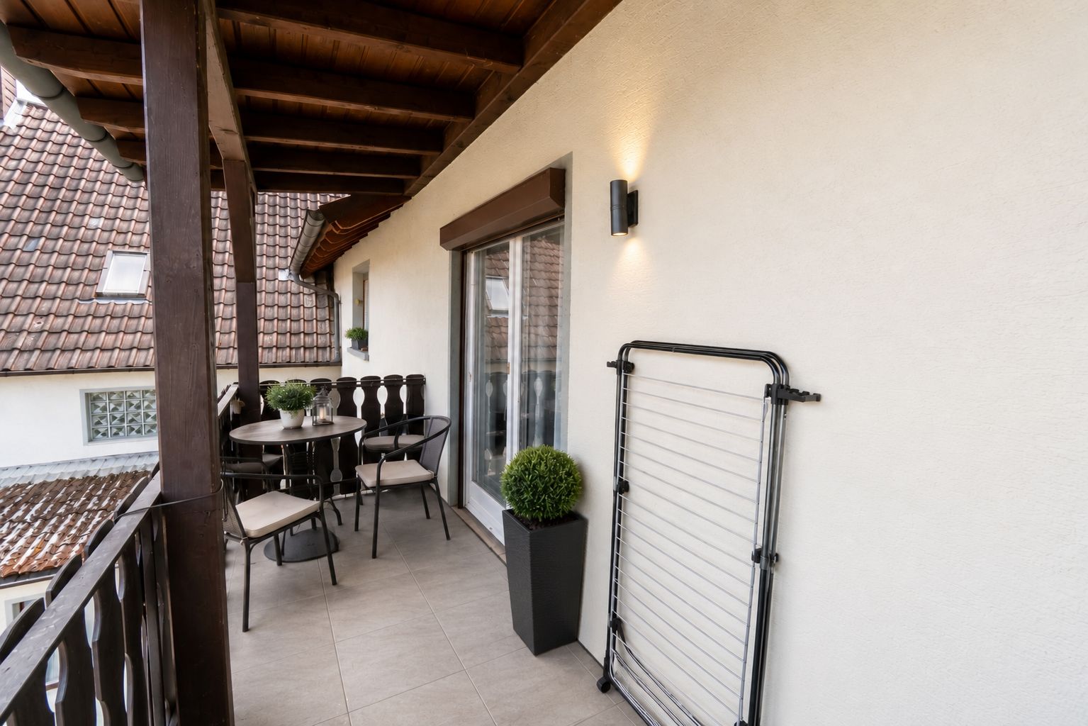 Überdachter Balkon mit Tisch, Stühlen, Pflanzen und Wäschetrockner an der Wand.
