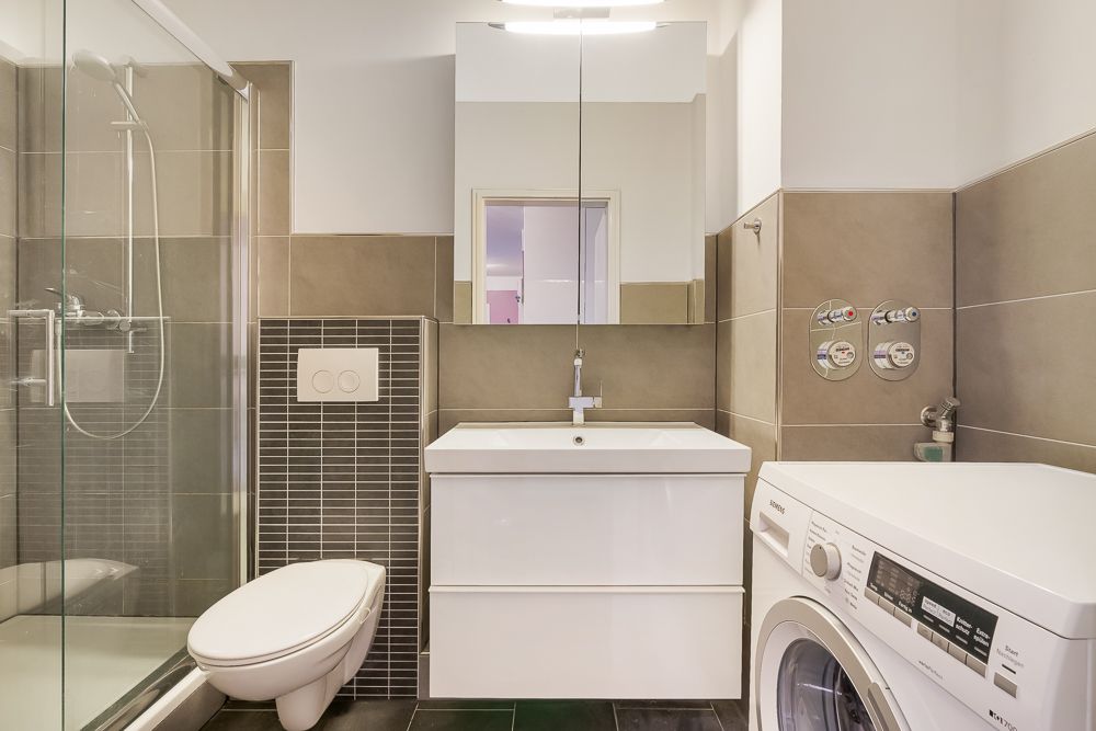 Modernes Badezimmer mit Dusche, Wandtoilette, Waschbecken und Waschmaschine.