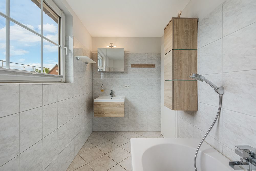 Modernes Badezimmer mit Badewanne, Waschbecken, großem Fenster und Holzschränken.