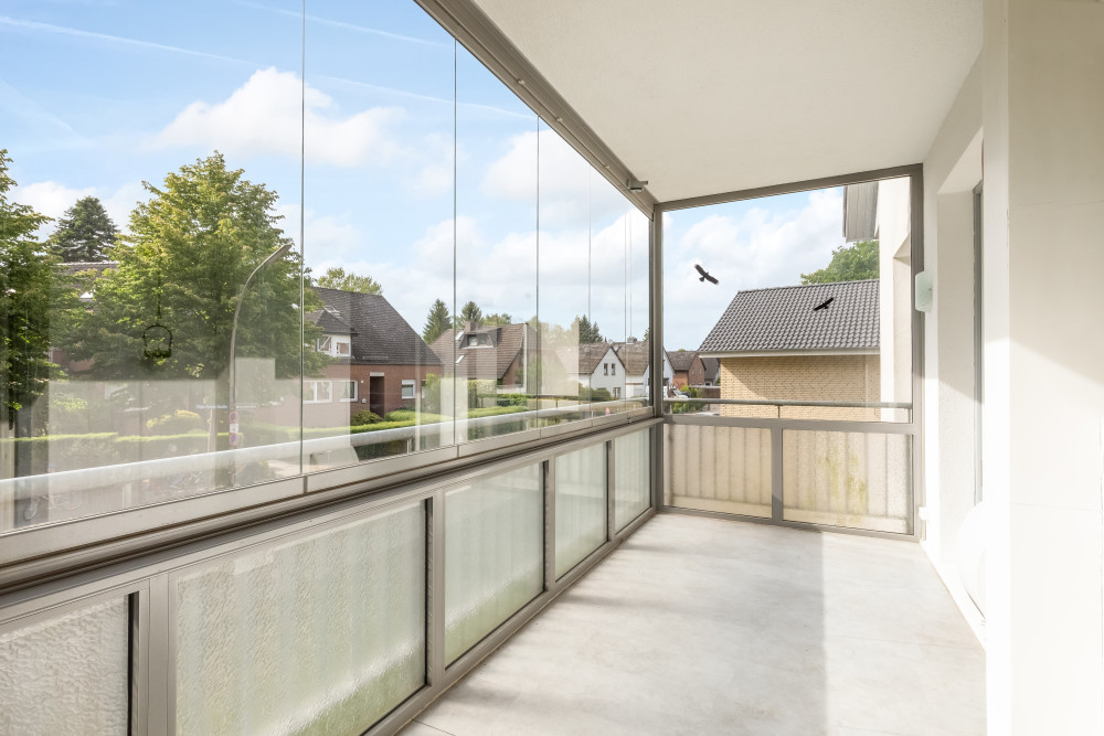 Überdachter Balkon mit Glaswänden und Blick auf Wohnhäuser und Bäume.