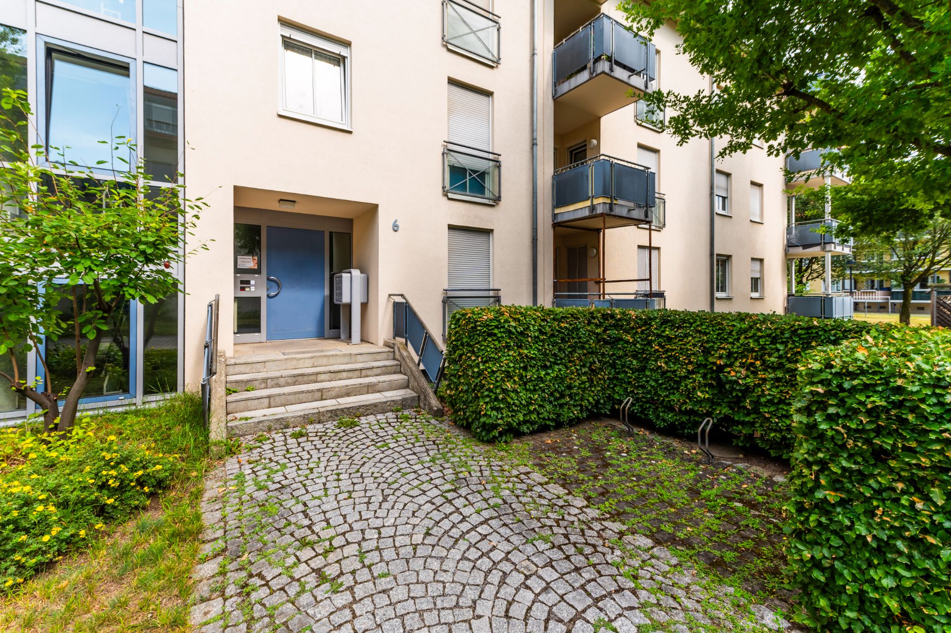 Eingangsbereich eines Mehrfamilienhauses mit Treppe, Briefkästen und Grünflächen.