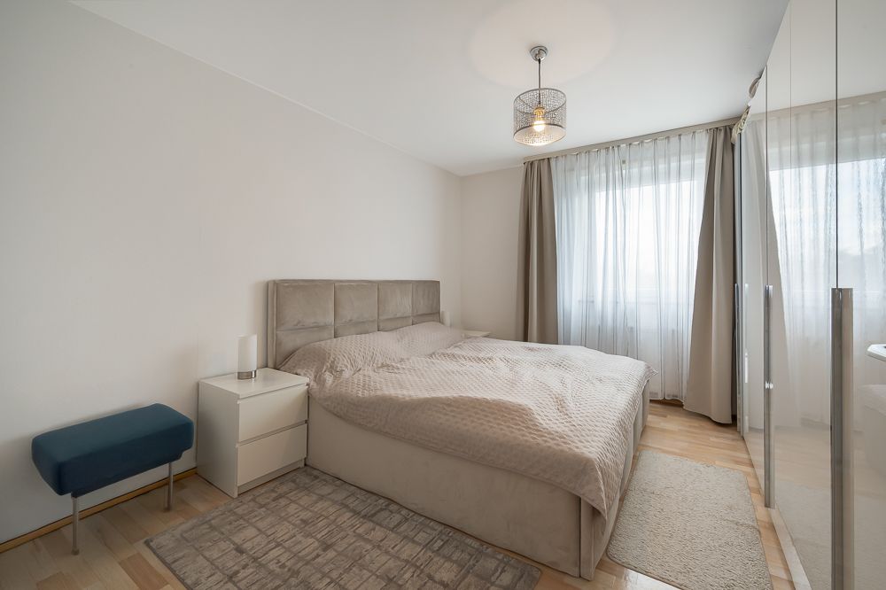 Helles Schlafzimmer mit Doppelbett, Nachttisch, Spiegel-Schrank und Fenster mit Vorhängen.