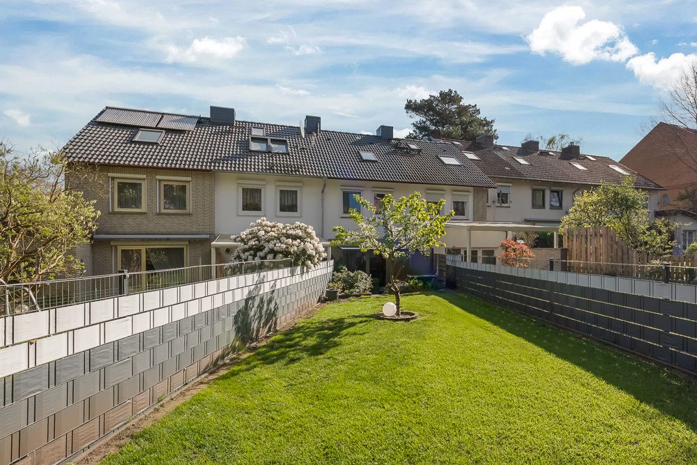Reihenhaus mit gepflegtem Garten, grünem Rasen und einigen Bäumen im Vordergrund.