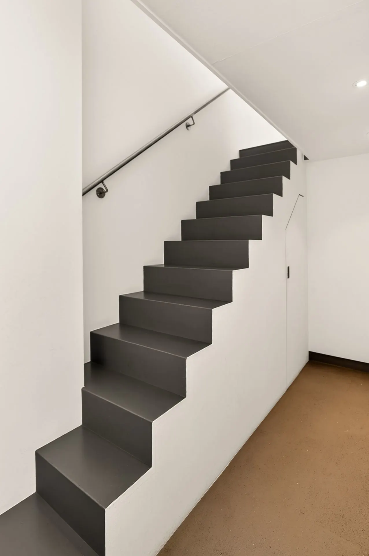 Moderne, graue Treppe mit Handlauf und Stauraum unter den Stufen in einem hellen Flur.