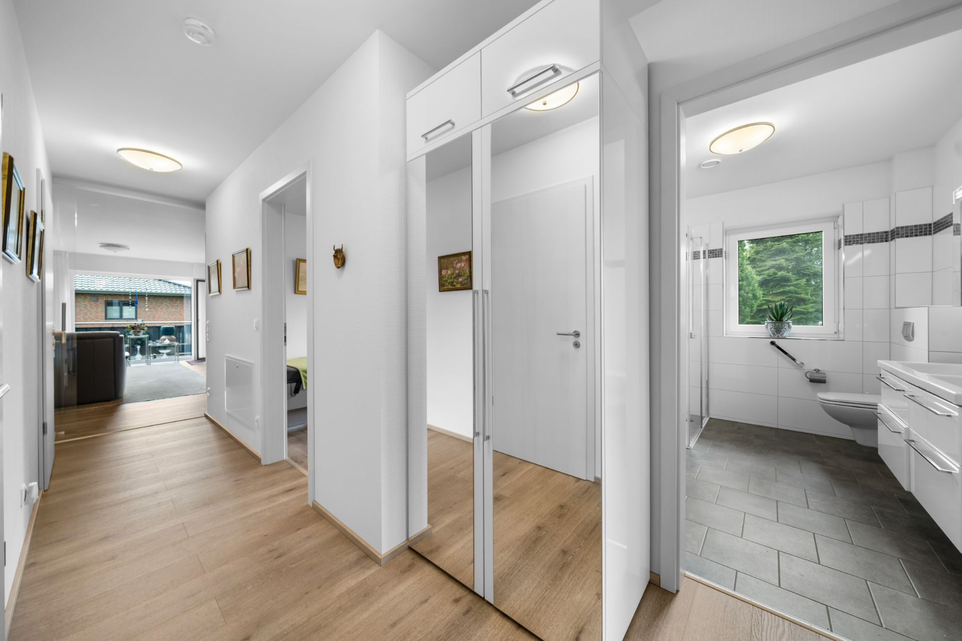 Heller Flur mit Spiegel-Schrank, Holzfußboden und Zugang zu einem modernen Bad mit Fenster.