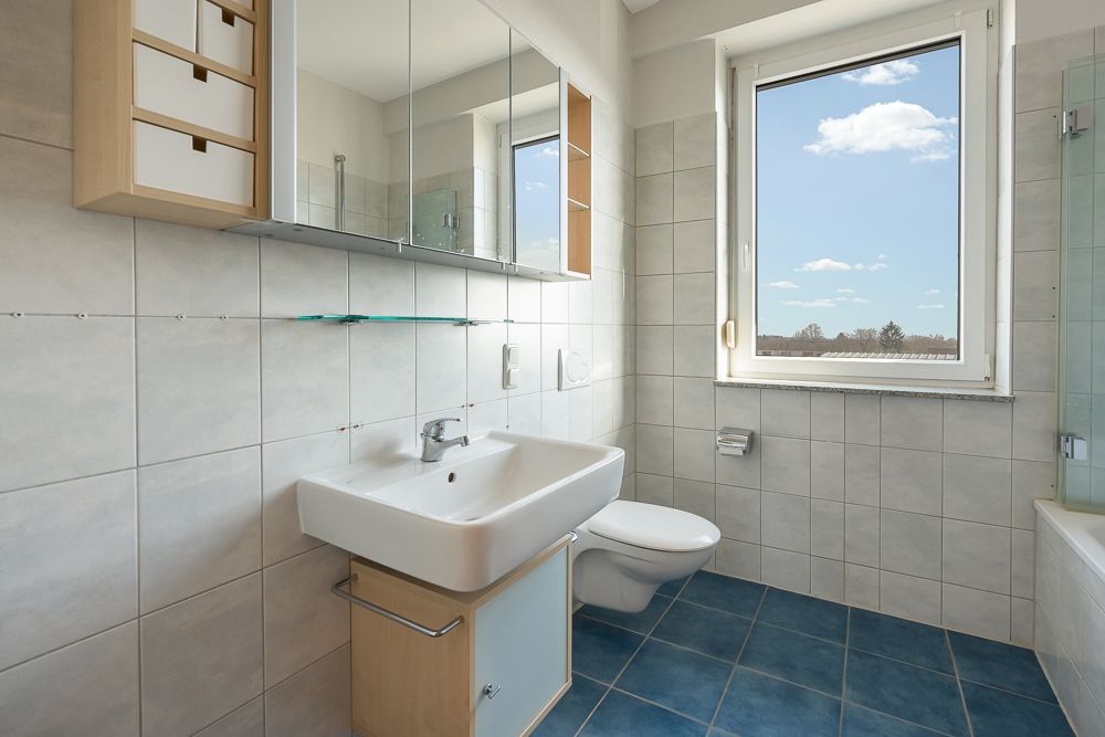 Modernes Badezimmer mit Waschbecken, Wandregal, Toilette und Fenster mit Ausblick.