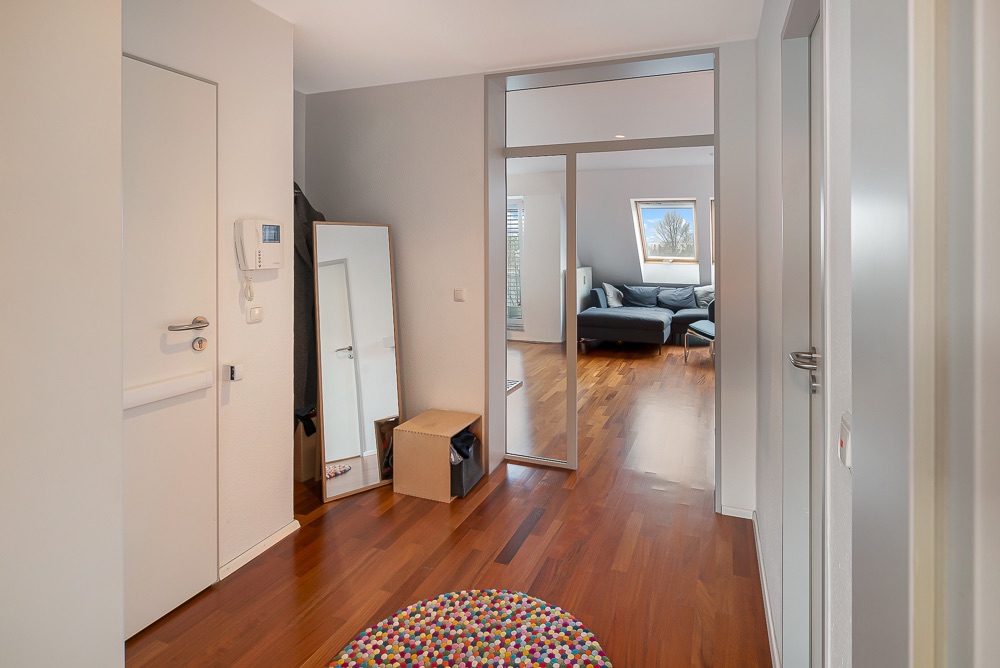 Moderner Flur mit Holzfußboden, rundem Teppich, Spiegel und Blick ins Wohnzimmer mit Sofa.