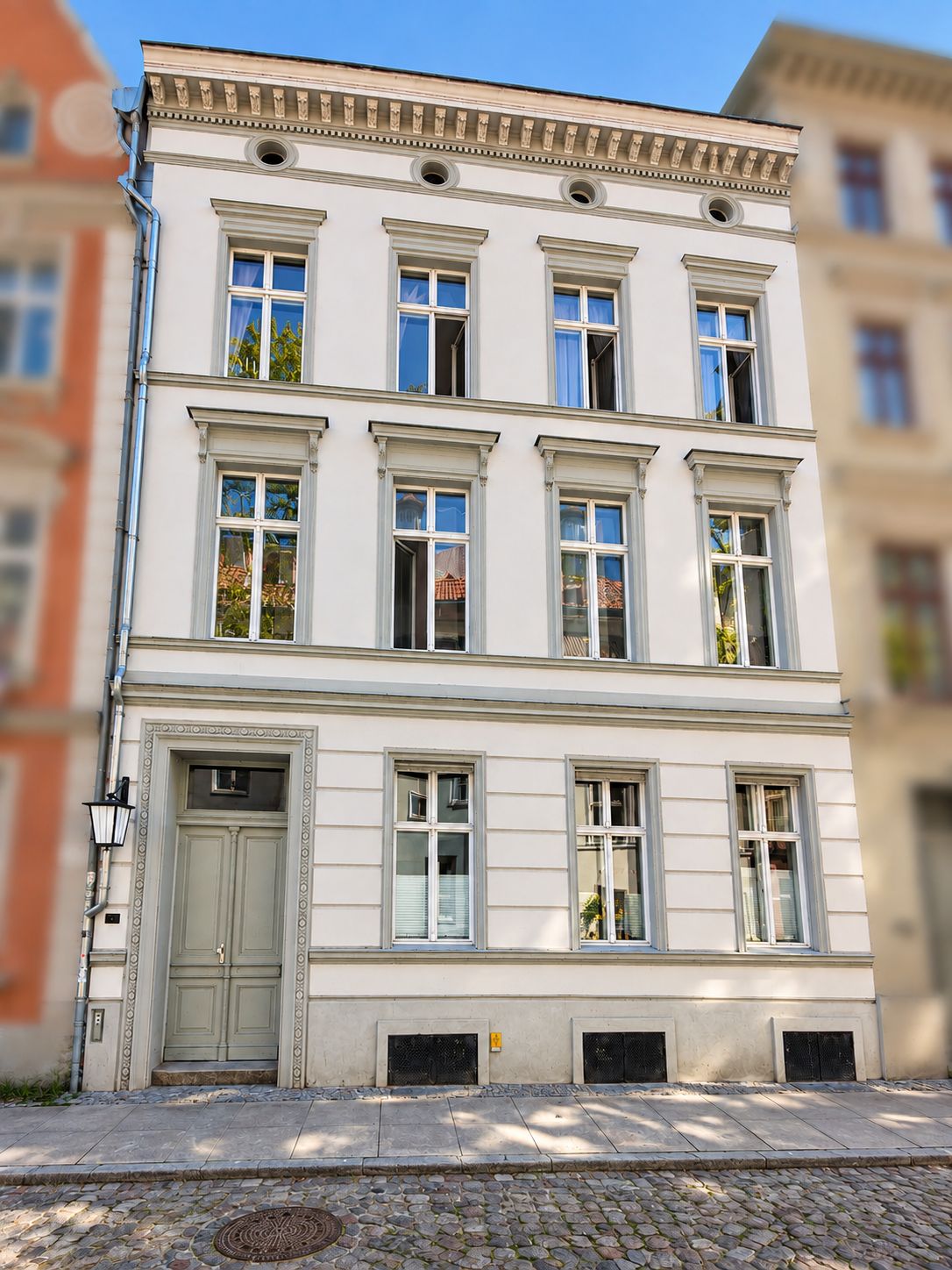 Dreistöckiges Wohnhaus mit neun Fenstern und einer Tür an einer gepflasterten Straße.