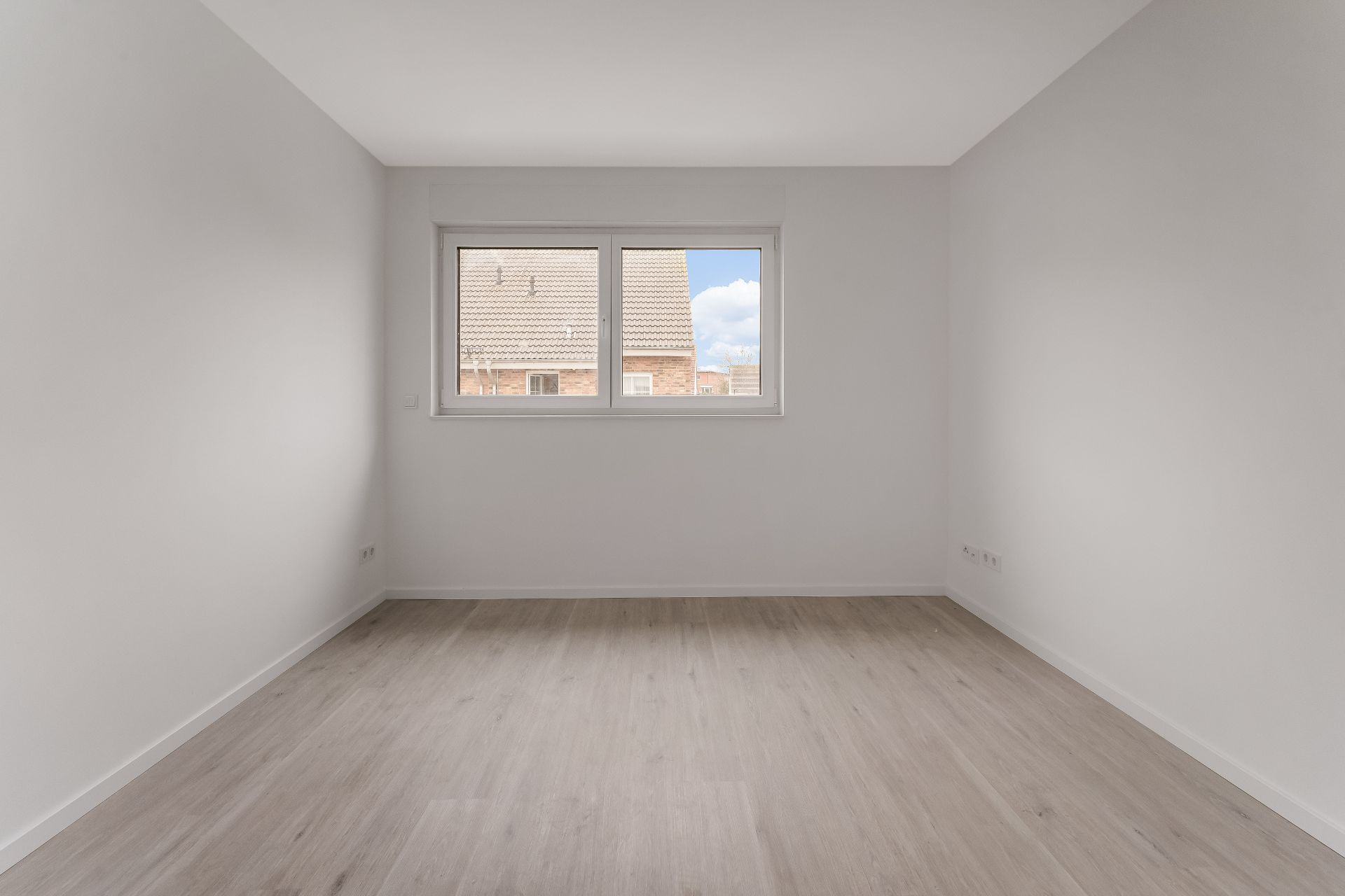 Leerer, heller Raum mit Holzfußboden und einem Fenster an der Stirnwand.