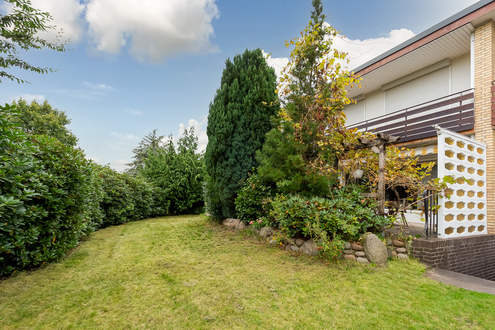 Gepflegter Garten mit Rasenfläche, Büschen und Bäumen neben einem Wohnhaus.