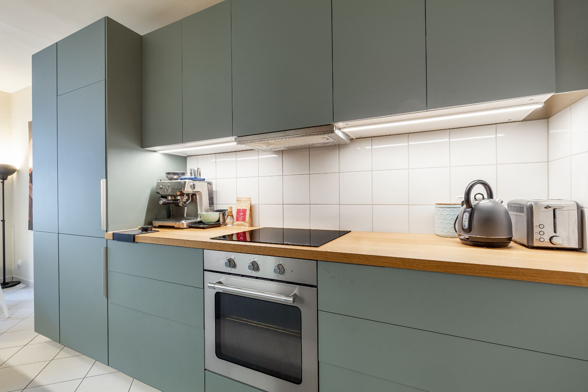 Moderne Küche mit grünen Schränken, Holzarbeitsplatte, Kaffeemaschine, Wasserkocher und Toaster.
