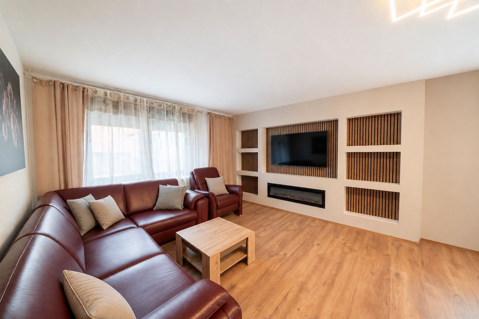 Wohnzimmer mit braunem Ecksofa, Sessel, Holztisch und Fernseher an der Wand.