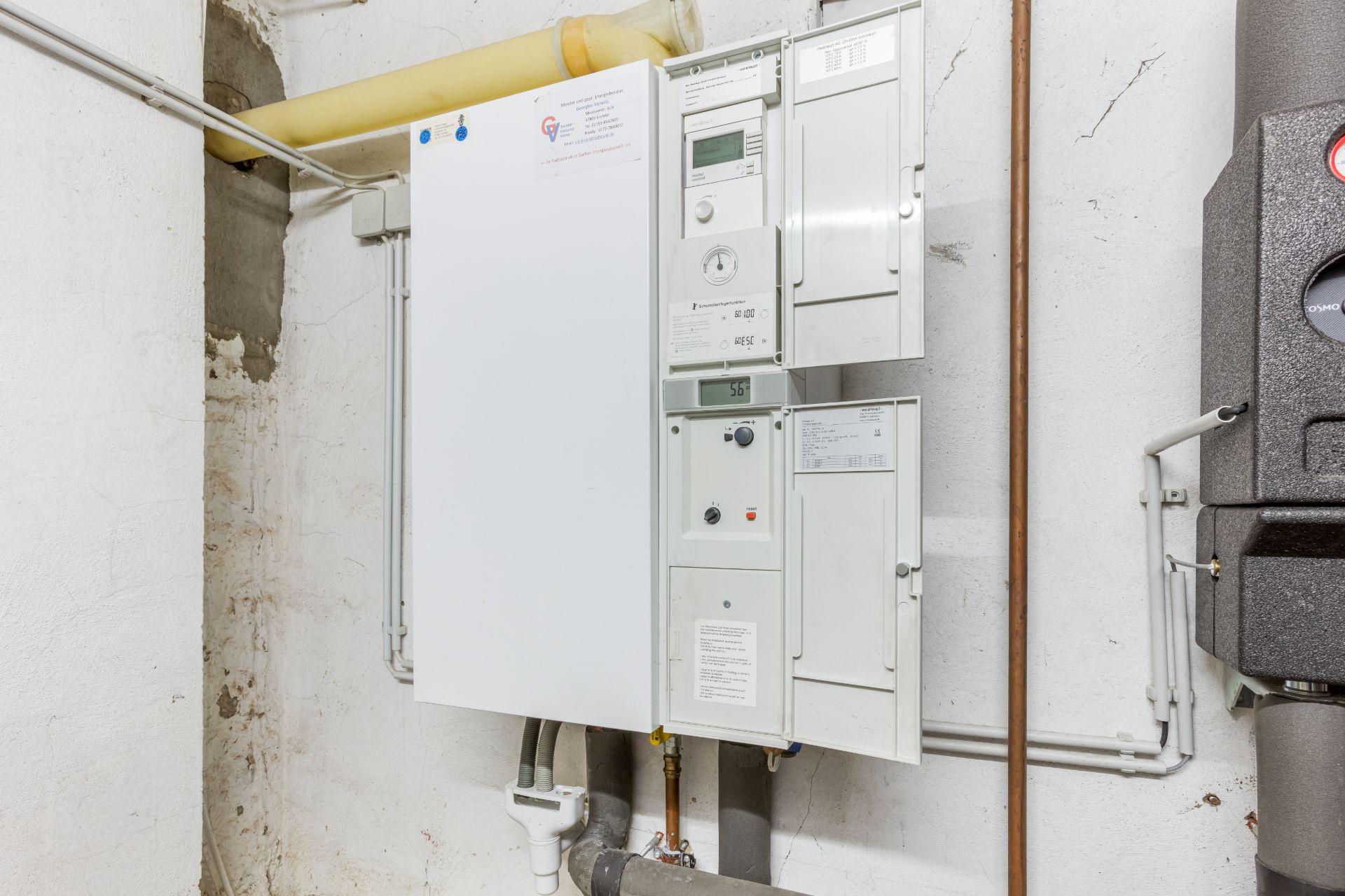 Ein Heizungs- oder Elektroschaltkasten an einer weißen Wand in einem Kellerraum.