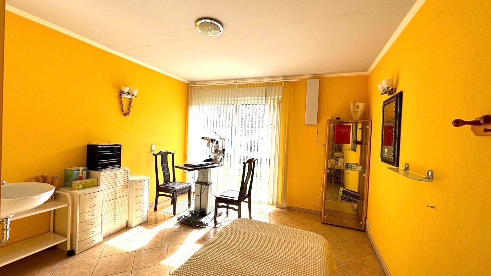 Helles Zimmer mit gelben Wänden, einem Bett, zwei Stühlen, Tisch, Spiegel und Waschbecken.