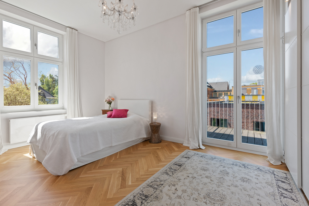 Helles Schlafzimmer mit Einzelbett, großem Teppich, Fenstern und Glastüren zum Balkon.