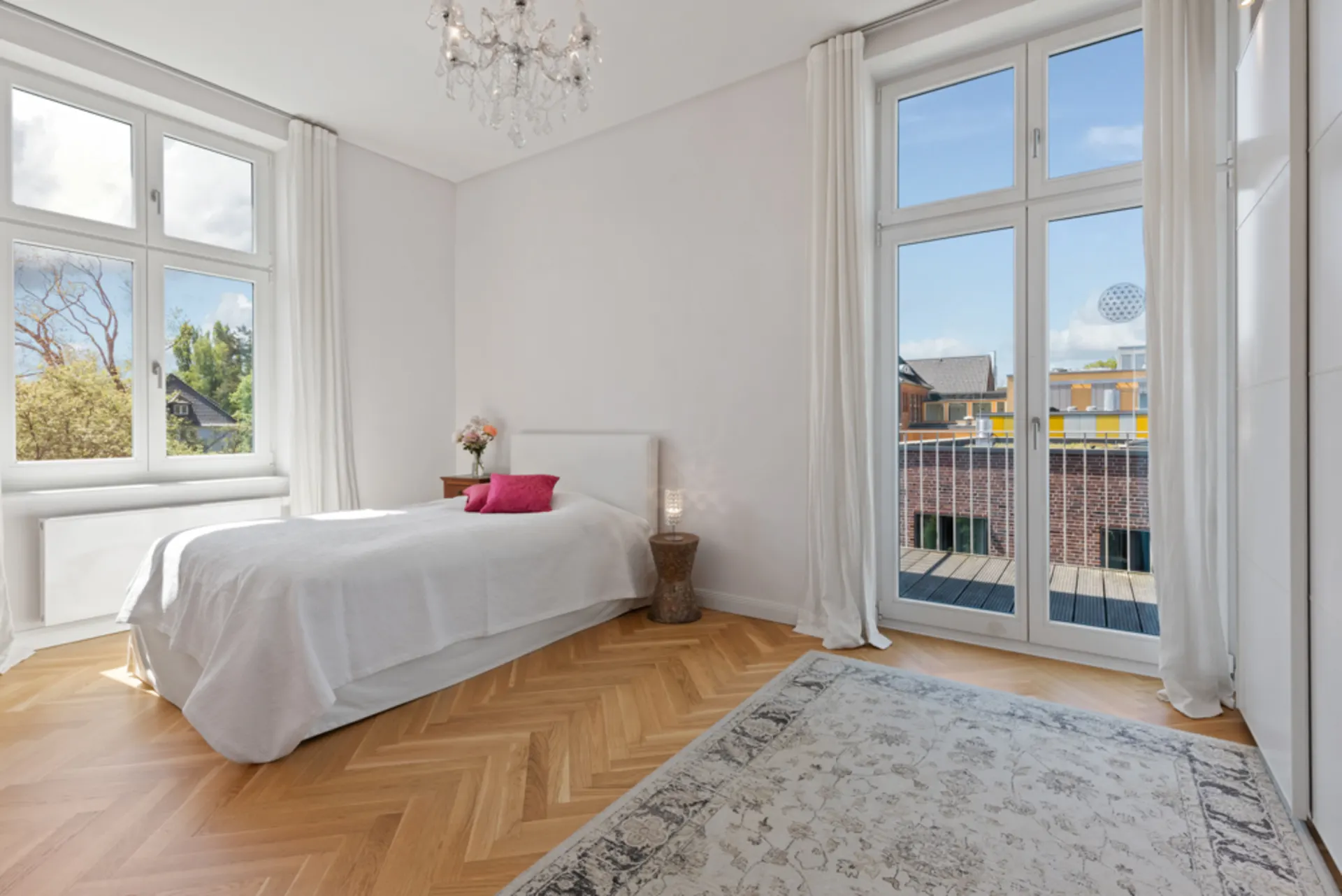 Helles Schlafzimmer mit Einzelbett, großem Teppich, Fenstern und Glastüren zum Balkon.