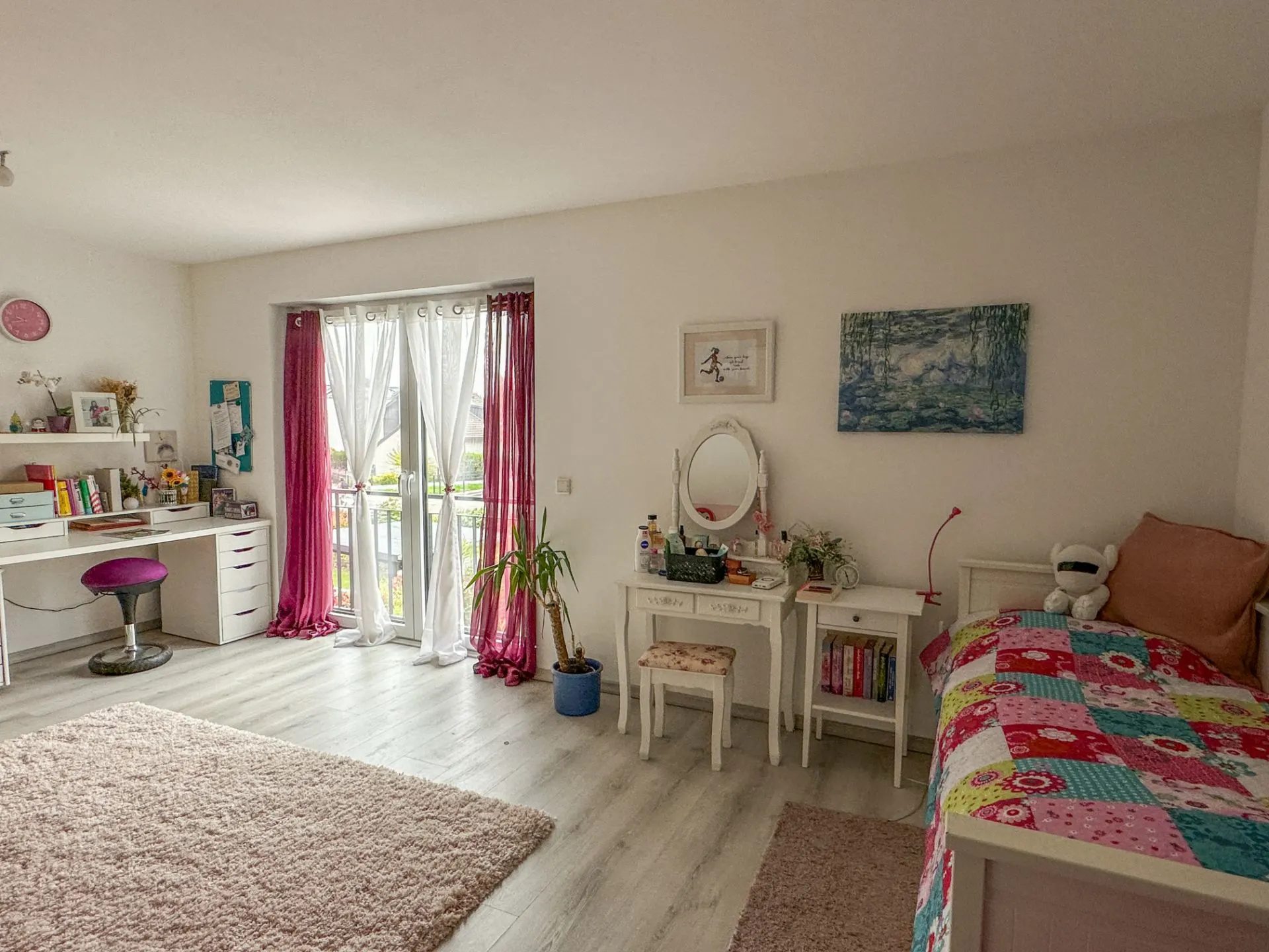 Helles Schlafzimmer mit Schreibtisch, Bett, Schminktisch und pinken Vorhängen an der Balkontür.