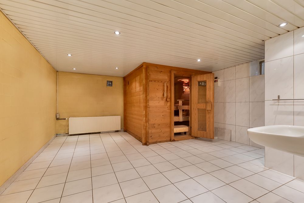 Heller Raum mit gefliestem Boden, Holzsauna, Waschbecken und Heizkörper.