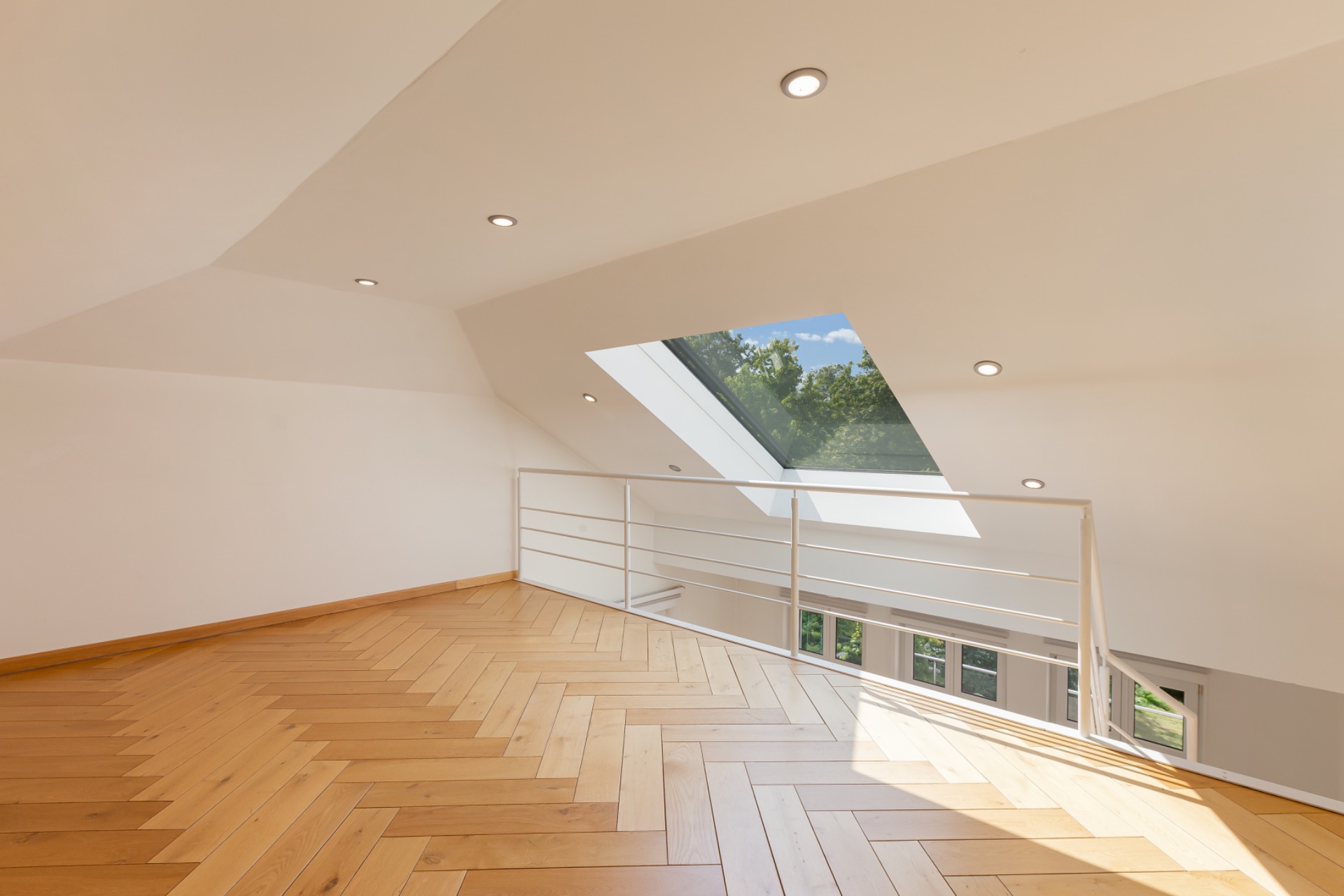 Helle Dachgeschossgalerie mit Holzfußboden, weißem Geländer und großem Dachfenster.