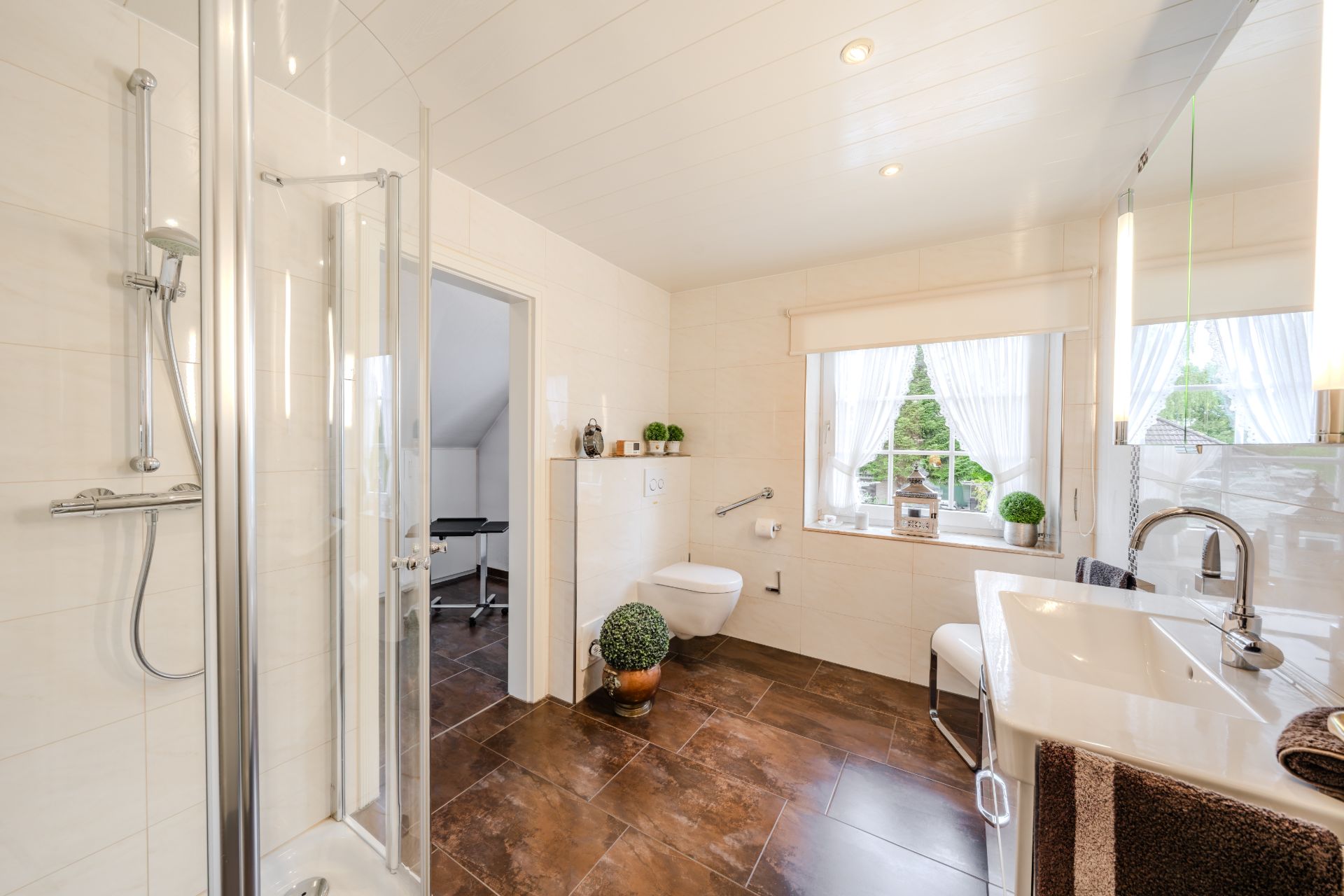 Modernes Badezimmer mit Dusche, Toilette, Waschbecken und großem Fenster mit Blick ins Grüne.