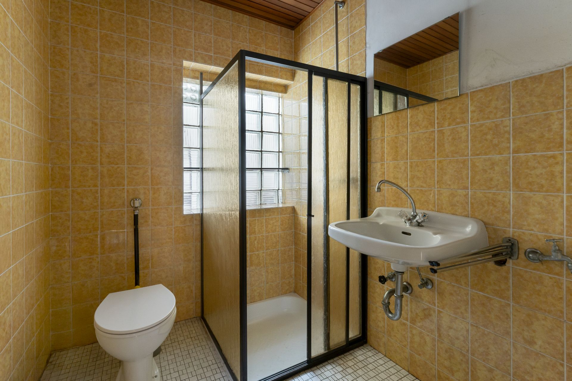 Badezimmer mit gelben Fliesen, Dusche mit Glastür, WC und Waschbecken.