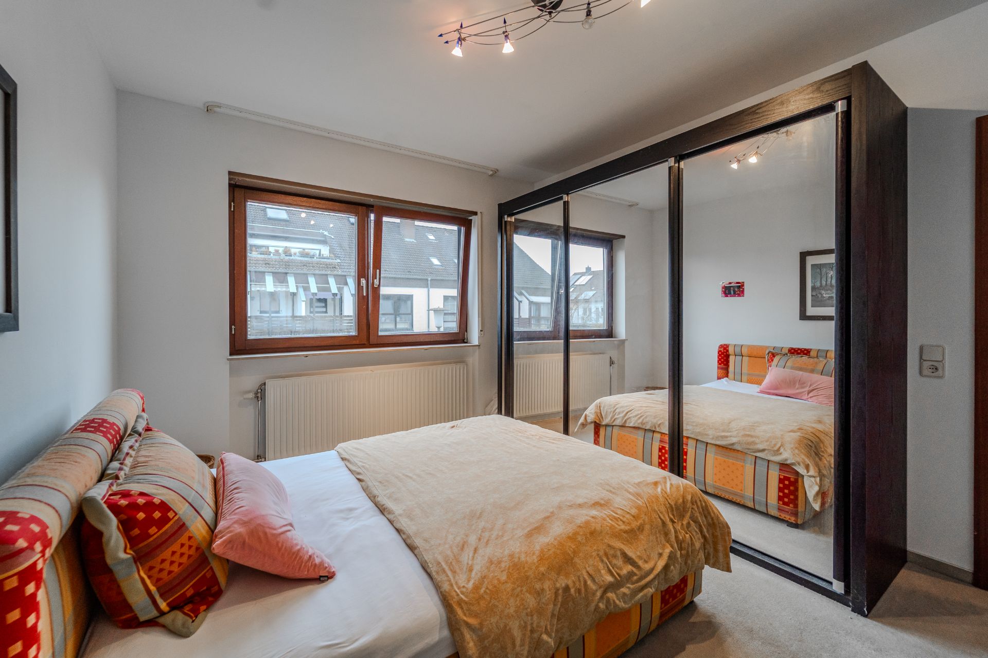 Schlafzimmer mit Doppelbett, bunten Kissen und großem Spiegel-Kleiderschrank.