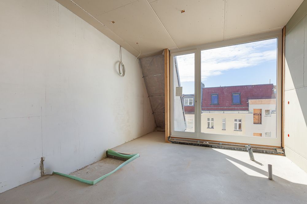 Leerer, unfertiger Raum mit großem Fenster und Blick auf Häuser gegenüber.