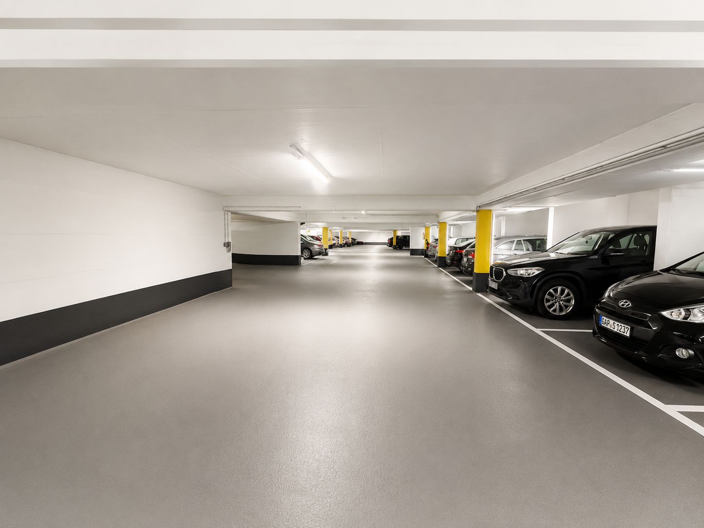Helle Tiefgarage mit geparkten Autos entlang der rechten Seite und gelben Pfeilern.