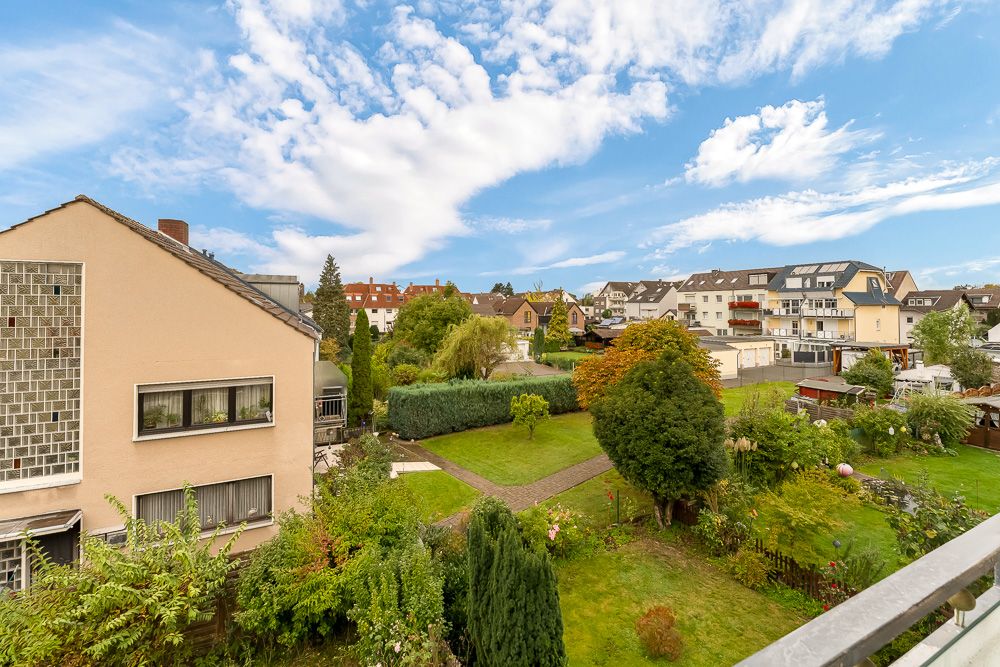 Blick auf einen gepflegten Garten mit Bäumen und Sträuchern sowie benachbarte Wohnhäuser.