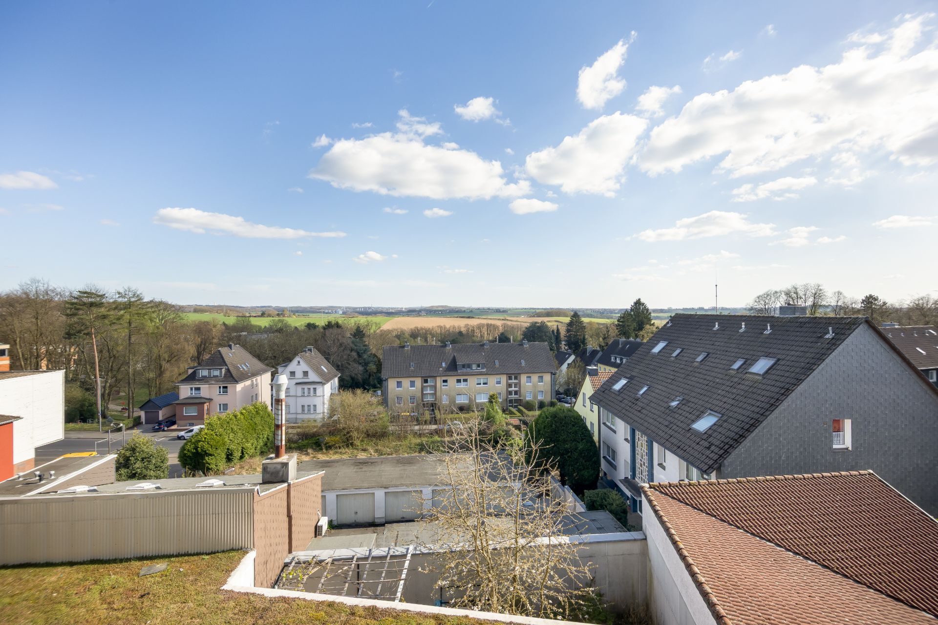 Blick auf Wohnhäuser, Garagen und Bäume unter blauem Himmel mit Wolken.