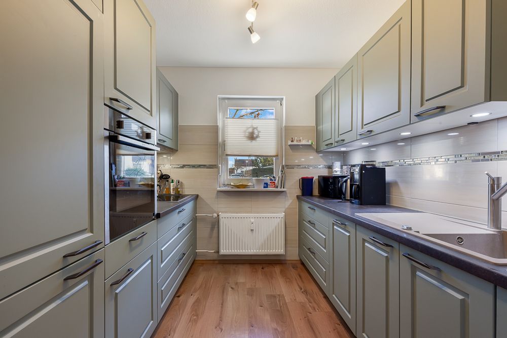Moderne Küche mit grauen Schränken, Holzfußboden und einem Fenster über der Heizung.