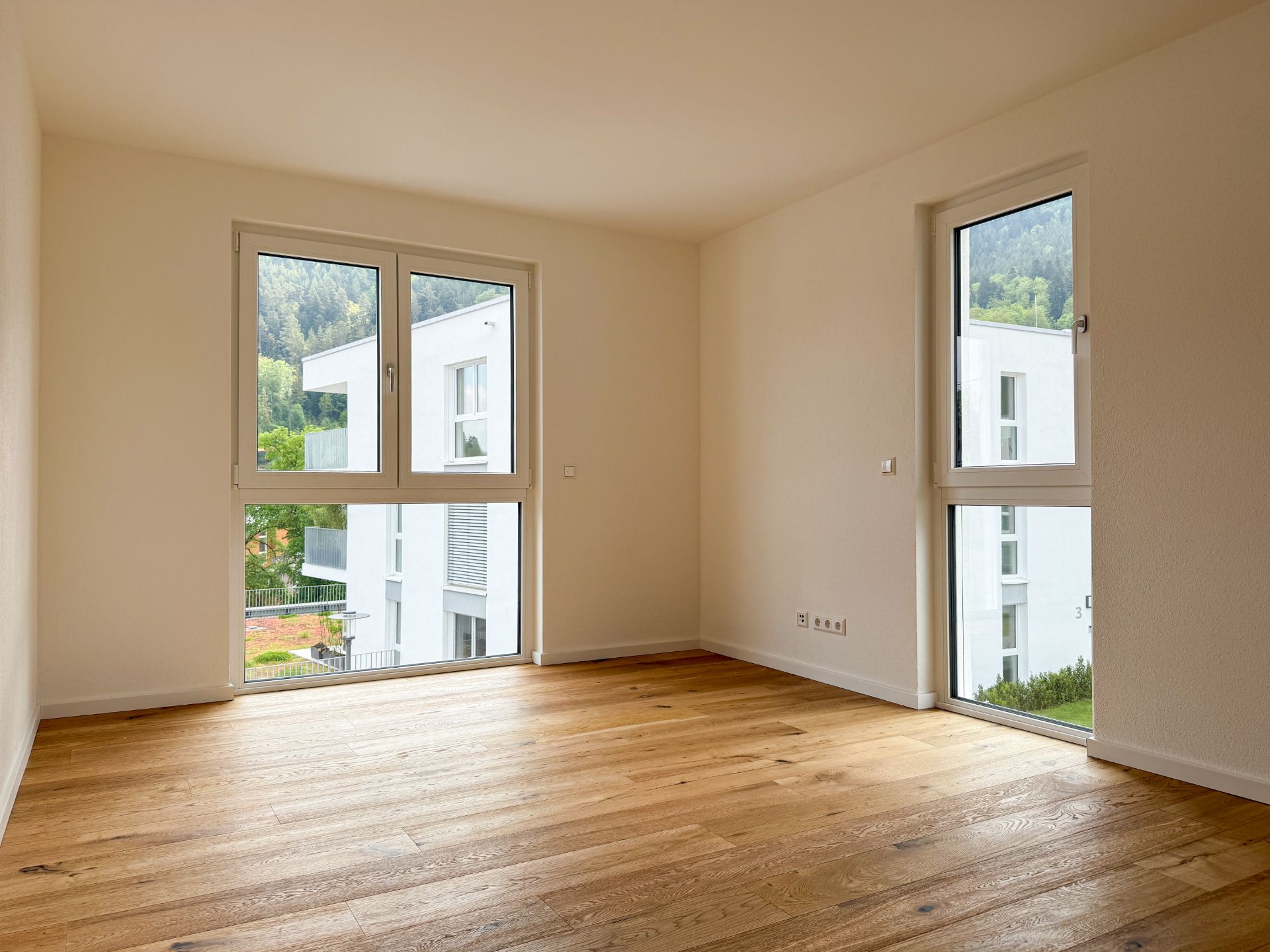 Leerer Raum mit Holzfußboden und großen Fenstern, Blick auf moderne Wohngebäude.