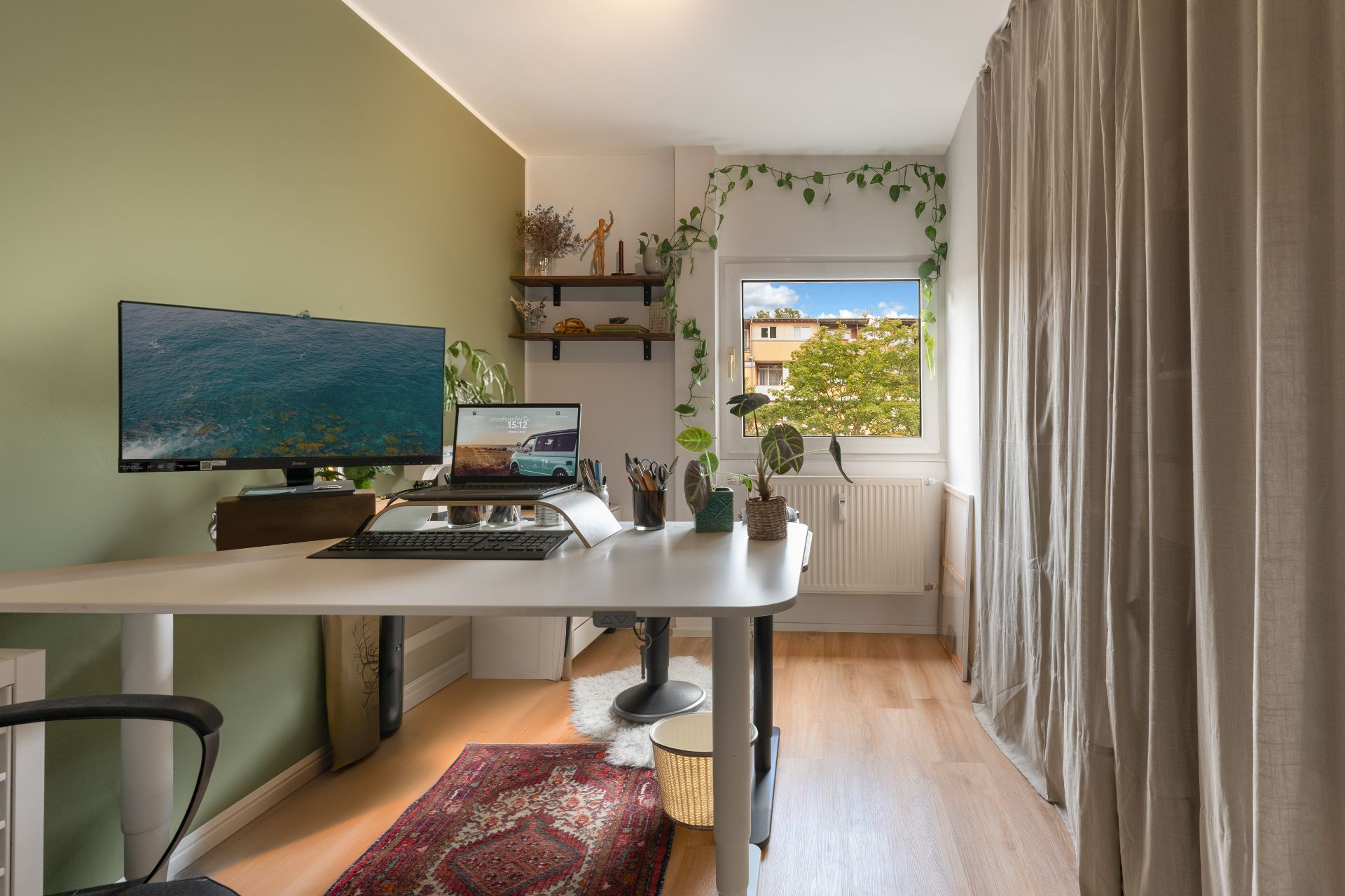 Modernes, helles Arbeitszimmer mit Schreibtisch, Monitoren, Pflanzen und Teppich am Fenster.