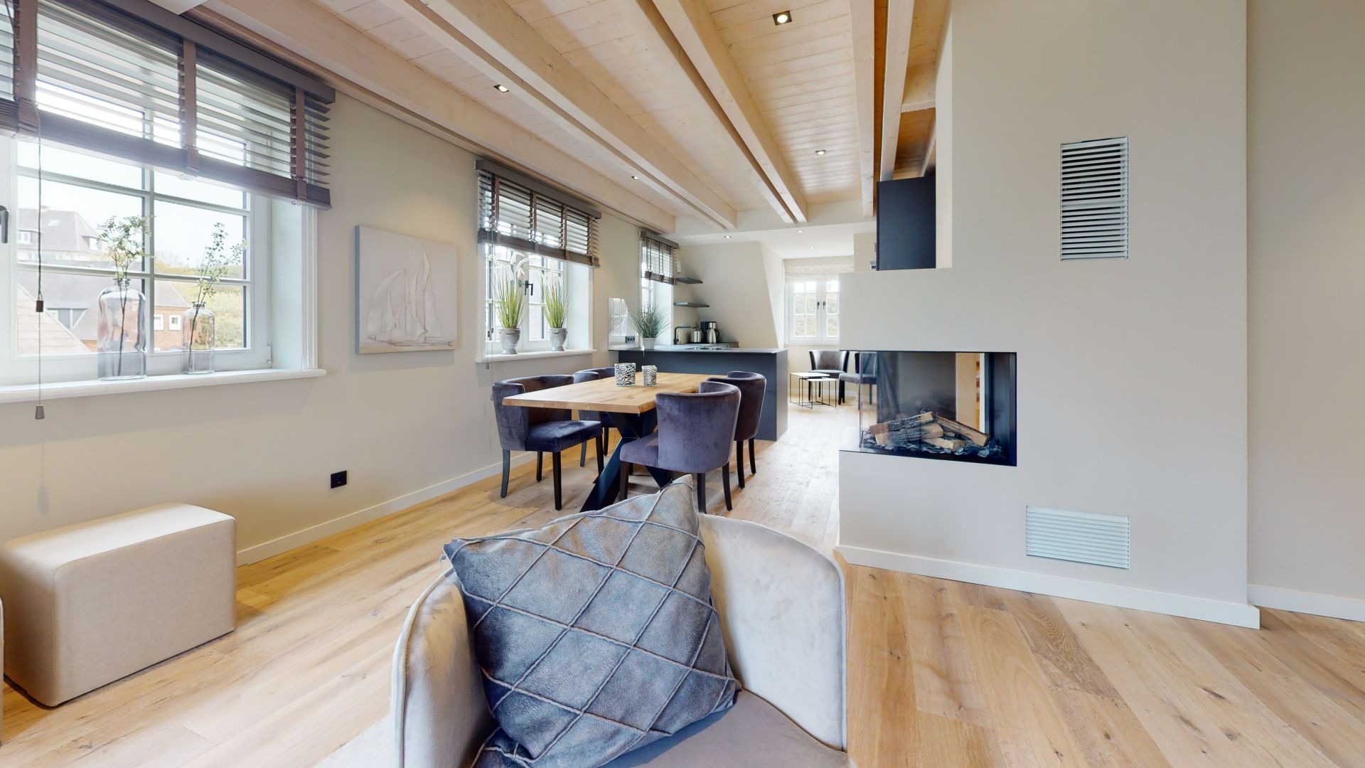 Helles Wohnzimmer mit Holzboden, Esstisch, Kamin und großen Fenstern.
